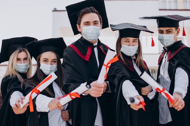 Gruppo di studenti che festeggiano insieme la laurea e indossano maschere per il viso