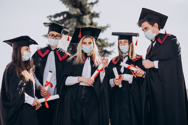 Gruppo di studenti che festeggiano insieme la laurea e indossano maschere per il viso