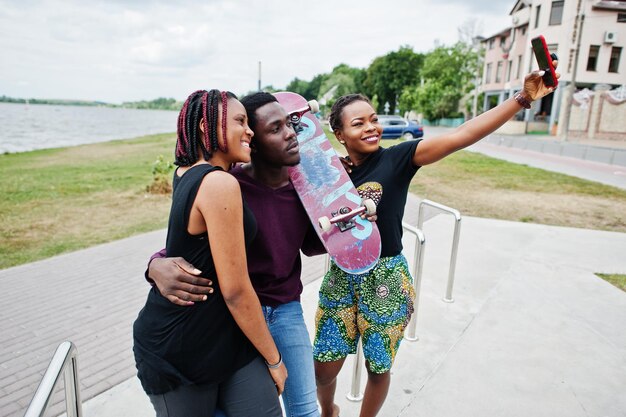 Gruppo di tre amici afroamericani con skateboard che fanno selfie sul telefono