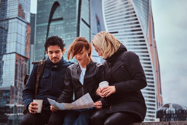 Gruppo di turisti che cercano un posto sulla mappa seduti con un caffè da asporto davanti ai grattacieli della città di Mosca.