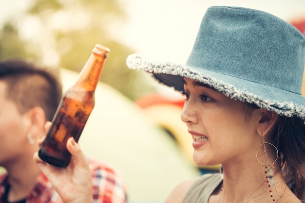 Gruppo di uomo e donna godono picnic camping e barbecue al lago con tende in background. Giovane razza mista razza asiatica donna e uomo. Le mani dei giovani tostano e applaudono la birra. Immagine filtrata dall&#39;annata