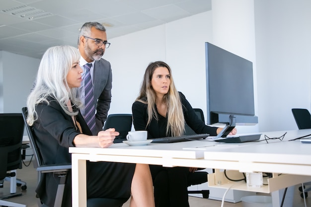 Gruppo focalizzato di affari che fissa al monitor del pc, guardando la presentazione del progetto sul posto di lavoro. Concetto di comunicazione aziendale