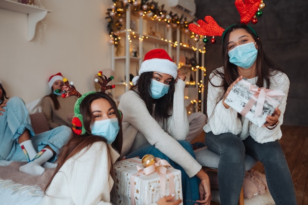 Gruppo multietnico di amici in cappelli di Babbo Natale sorridenti e in posa per la telecamera con doni nelle mani. Il concetto di celebrare il nuovo anno e il Natale sotto le restrizioni del coronavirus. vacanza in quarantena