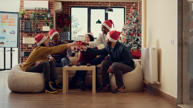 Gruppo multietnico di persone che tintinnano bicchieri di vino per fare un brindisi alla vigilia di Natale. Dire applausi e bere alcolici per celebrare l'evento delle vacanze invernali, una festa festosa in ufficio.