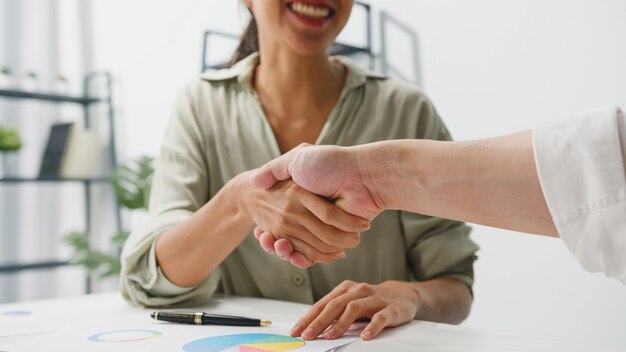 Gruppo multirazziale di giovani creativi in abbigliamento casual intelligente che discutono di affari che si stringono la mano insieme