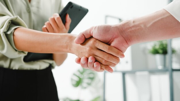 Gruppo multirazziale di giovani creativi in abbigliamento casual intelligente che discutono di affari che si stringono la mano insieme