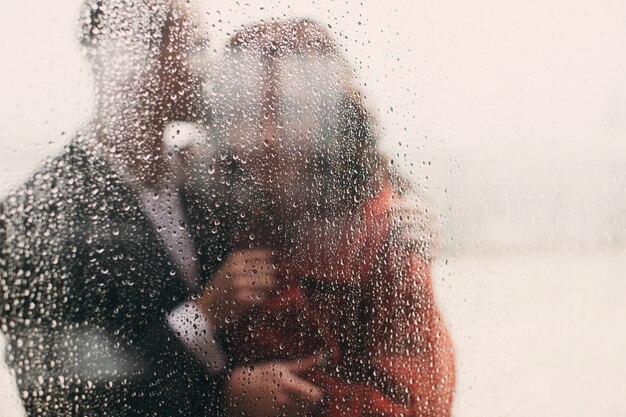 Guarda attraverso la finestra bagnata a abbracciare coppia