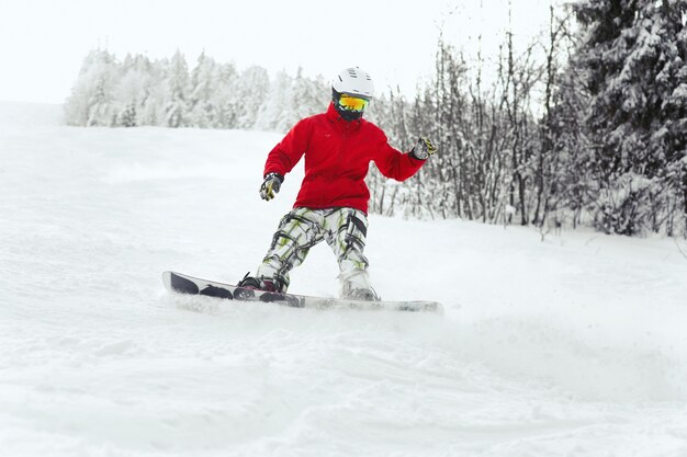 Guarda da sotto l&#39;uomo che scende sullo snowboard lungo la linea della foresta