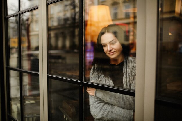 Guarda dall&#39;esterno una donna affascinante in piedi pensierosa dietro la finestra