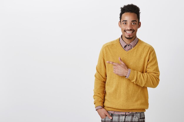 Guarda questa ragazza sexy. Ritratto di felice bell'uomo africano con taglio di capelli afro in elegante maglione giallo rivolto a sinistra e sorridente positivamente, essendo soddisfatto discutendo un concetto interessante