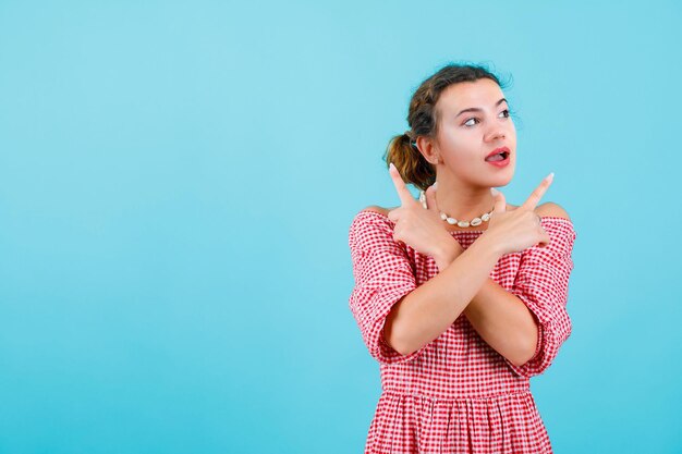 Guardando a sinistra la ragazza sta incrociando le mani e puntando verso l'alto con gli indici su sfondo blu