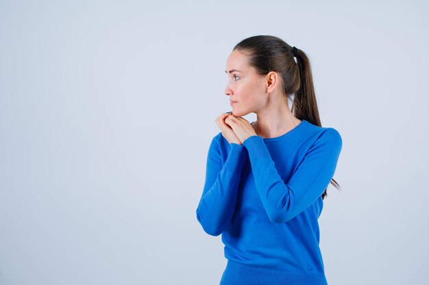 Guardando a sinistra la ragazza sta mettendo le mani sotto il mento su sfondo bianco