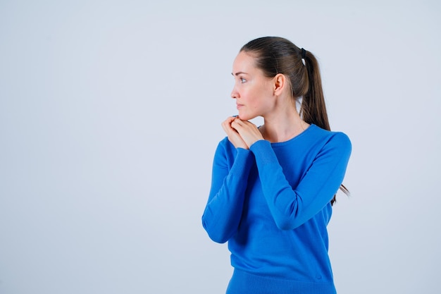 Guardando a sinistra la ragazza sta mettendo le mani sotto il mento su sfondo bianco