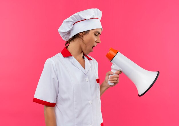 Guardando giù la giovane cuoca che indossa l'uniforme del cuoco unico parla sull'altoparlante sulla parete rosa isolata con lo spazio della copia