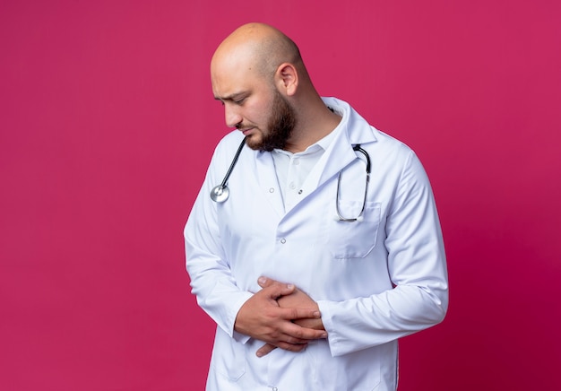 guardando giù triste giovane medico maschio che indossa veste medica e stetoscopio afferrò lo stomaco