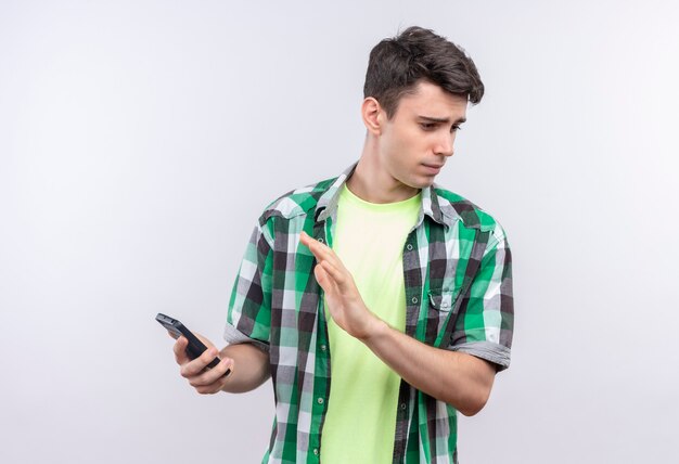 Guardando il giovane caucasico laterale che indossa la camicia verde non sembra una telefonata sul muro bianco isolato