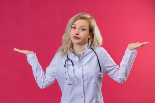 Guardando il giovane medico che indossa lo stetoscopio in abito medico diffonde le mani su sfondi rossi