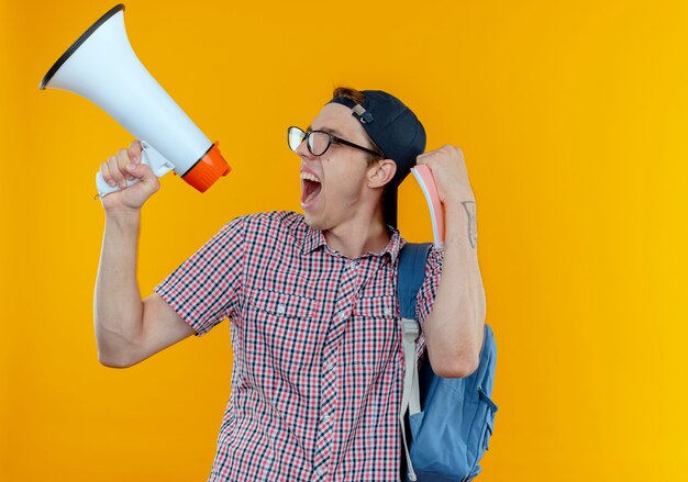 Guardando il lato gioioso giovane studente che indossa borsa, occhiali e berretto parla all'altoparlante e mostra un gesto di sì