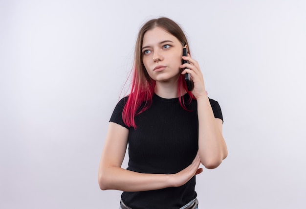 Guardando il lato giovane bella ragazza che indossa la maglietta nera parla al telefono su sfondo bianco isolato