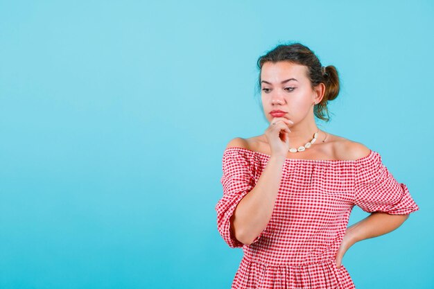 Guardando in basso la ragazza sta pensando tenendo una mano sul mento e l'altra sulla vita su sfondo blu