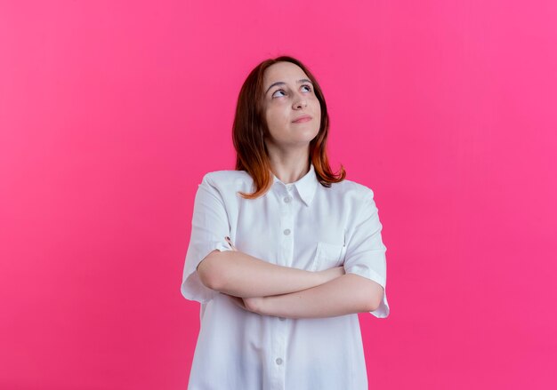 Guardando le mani incrociate felice giovane ragazza rossa isolato su sfondo rosa