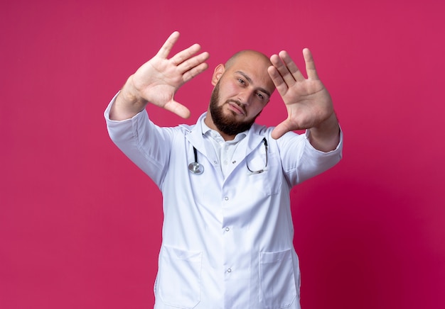 Guardando un giovane medico maschio calvo che indossa una tunica medica e uno stetoscopio che tende la mano alla telecamera