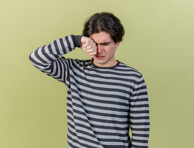 Guardando verso il basso piangendo giovane uomo malato asciugandosi gli occhi con la mano isolata su sfondo verde oliva