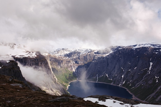 Guardi da sopra al lago blu fra le alte rocce in Norvegia