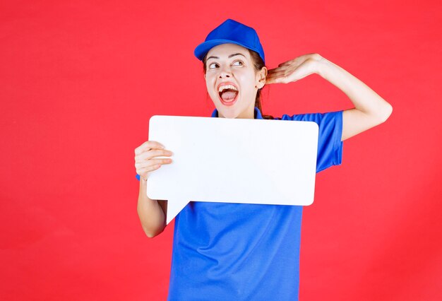 Guida femminile in uniforme blu che tiene in mano un pannello informativo rettangolare bianco e apre le orecchie e urla.