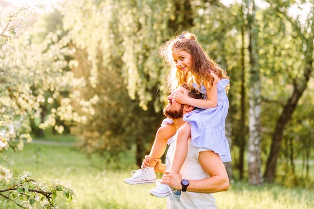 Guida sorridente della bambina sulle spalle del padre nel parco