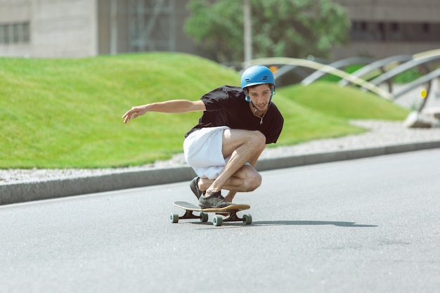 Guidatore di skateboard facendo un trucco per la strada della città in una giornata di sole. Giovane uomo in attrezzatura equitazione e longboard sull'asfalto in azione. Concetto di attività per il tempo libero, sport, estremo, hobby e movimento.