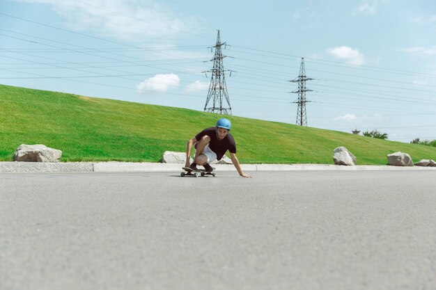 Guidatore di skateboard facendo un trucco per la strada della città in una giornata di sole. Giovane uomo in attrezzatura equitazione e longboard vicino a prato in azione. Concetto di attività per il tempo libero, sport, estremo, hobby e movimento.