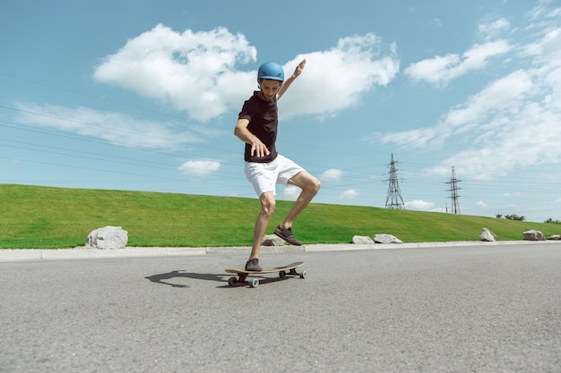 Guidatore di skateboard facendo un trucco sulla strada della città in una giornata di sole. Giovane uomo in attrezzatura equitazione e longboard vicino a prato in azione. Concetto di attività per il tempo libero, sport, estremo, hobby e movimento.