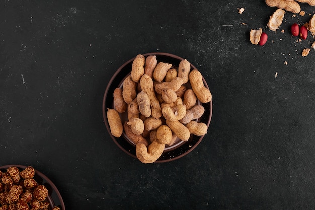 Gusci di arachidi in un piattino in ceramica isolato su uno spazio nero, vista dall'alto.