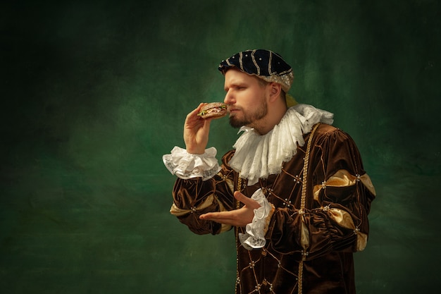 Gusto segreto. Ritratto di giovane medievale in abiti vintage con cornice in legno su sfondo scuro. Modello maschile come duca, principe, persona reale. Concetto di confronto di epoche, moderne, moda.