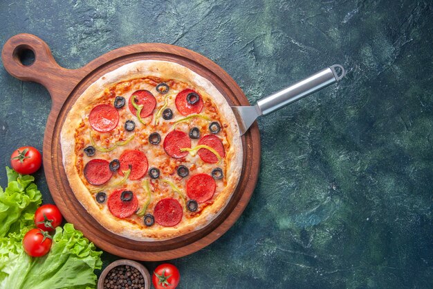 Gustosa pizza fatta in casa sul bordo di legno bottiglia di olio pomodori pepe verde fascio sulla superficie scura