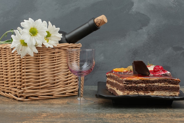 Gustosa torta con cesto e bottiglia sul tavolo di marmo.