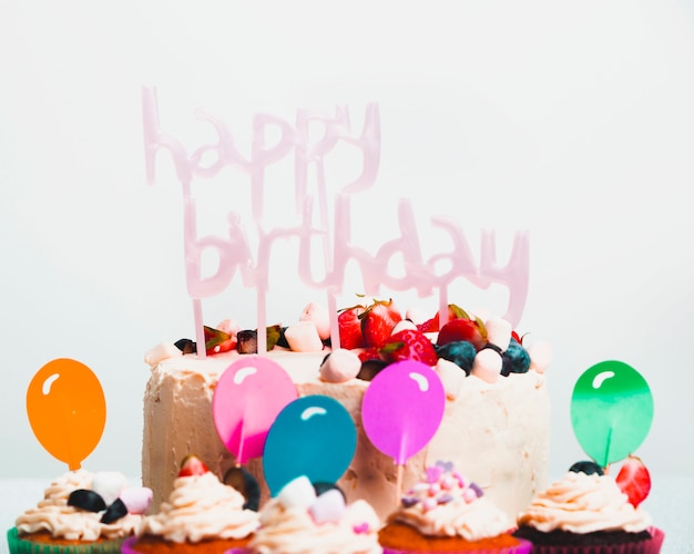 Gustosa torta fresca con frutti di bosco e titolo di buon compleanno vicino set di muffin