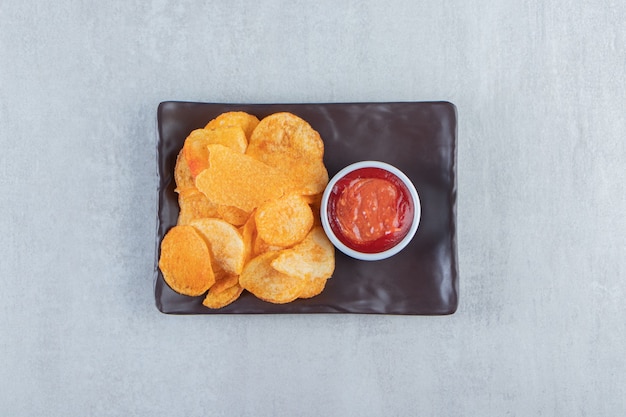 Gustose patatine speziate e ketchup posti su un piatto scuro.