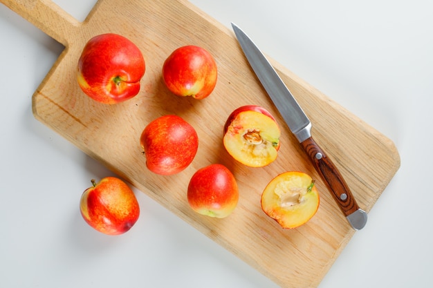 Gustose pesche con un coltello da frutta in un tagliere su superficie bianca, piatto disteso.