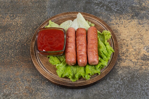 Gustose salsicce arrostite e ketchup su tavola di legno.