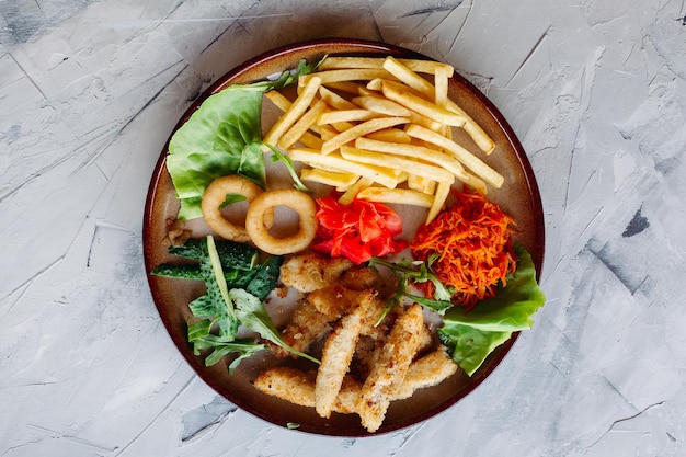 Gustosi antipasti da ristorante per grandi aziende tra cui pepite di pollo dorate patate fritte insalata verde foglie e cetrioli freschi In piedi su un tavolo bianco