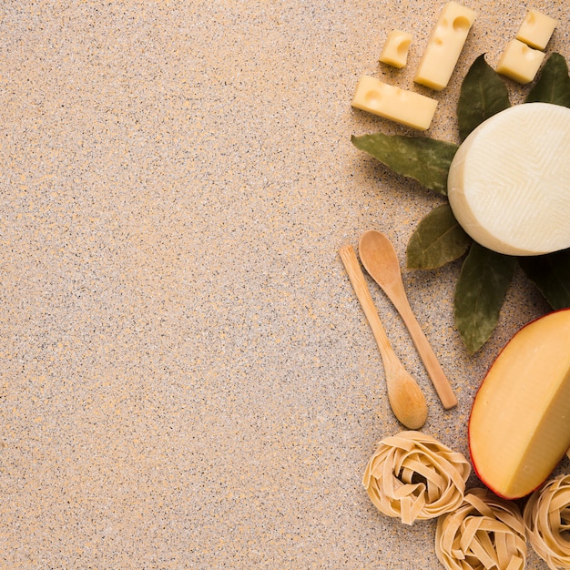 Gustosi tipi di formaggi freschi con pasta cruda; foglie di alloro e cucchiaio di legno sulla superficie di marmo texture