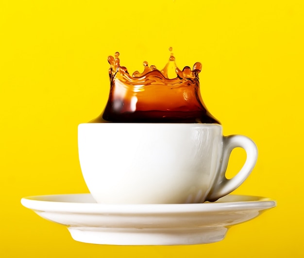 Gustoso caffè nero fresco nella tazza splash corona su sfondo vibrante giallo. Art Design