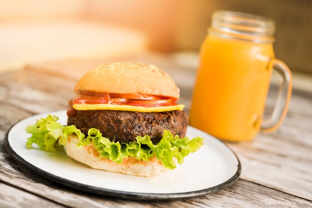 Hamburger con pomodori; formaggio e lattuga servito con bicchiere di succo sulla tavola di legno