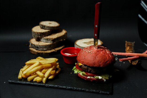 Hamburger di carne vista frontale con patatine ketchup e maionese su un supporto con un coltello