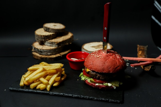 Hamburger di carne vista frontale con patatine ketchup e maionese su un supporto con un coltello