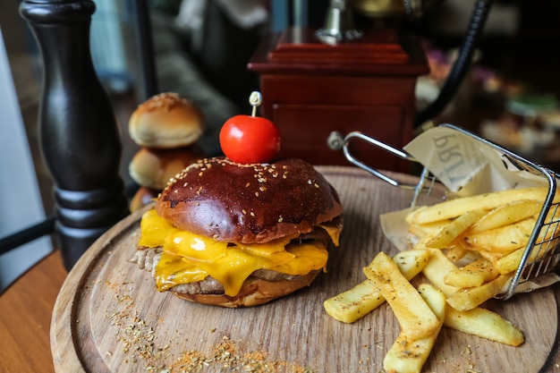 Hamburger di carne vista laterale con pomodoro e patatine fritte con spezie su un supporto