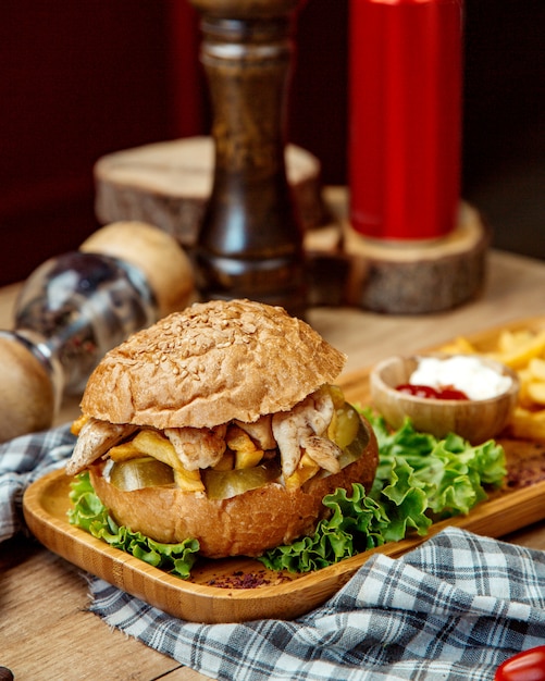 hamburger di pollo con ketchup, maionese e patatine fritte su un vassoio di legno