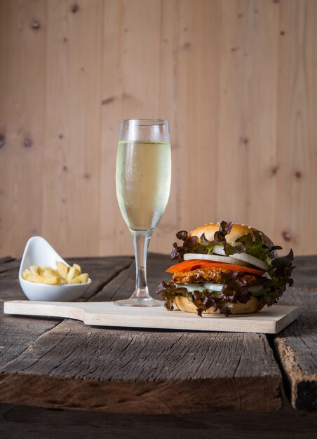 Hamburger di pollo fatto in casa con champagne, patatine fritte, lattuga, pomodoro e cipolla sulla tavola di legno.